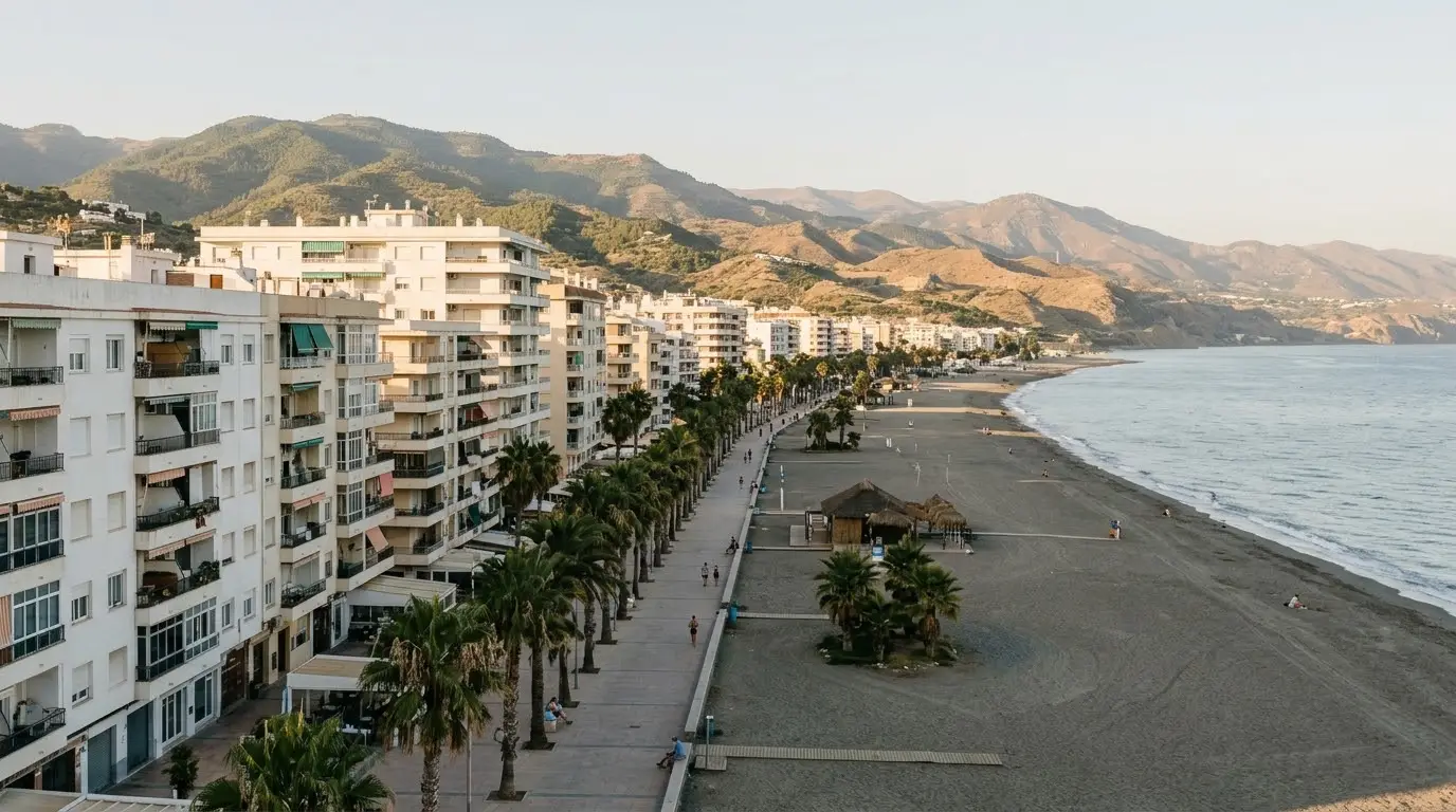 Paseo marítimo de Torre del Mar con edificios blancos de pisos, palmeras y la playa, con los montes de la Axarquía al fondo